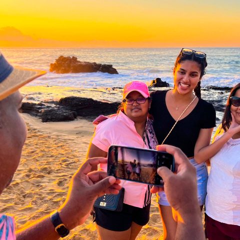 Group enjoying a sunrise photoshoot on an Oahu beach during a Hawaii tour, with golden sunlight and ocean waves in the background.