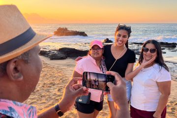 A man takes a picture of his family on the beach in Hawaii during the sunrise